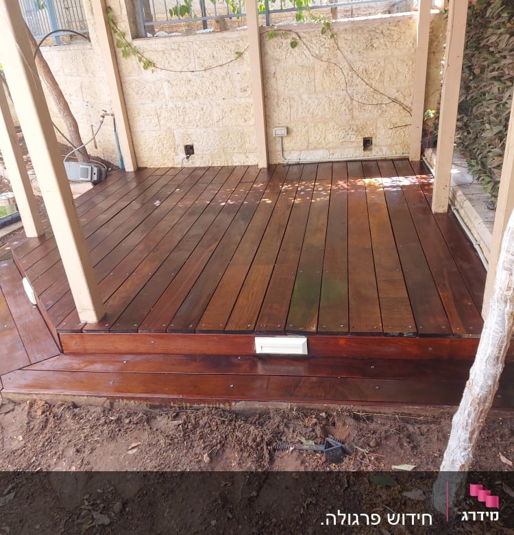 דק עץ בגינה עם עמודים וצמחייה מסביב